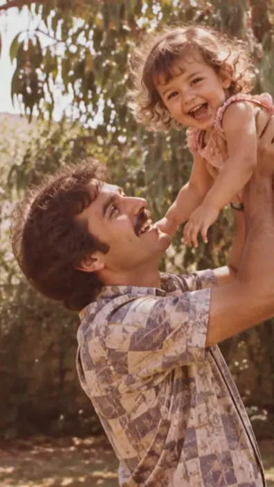 התמונה מ־1979: אב מרים את בתו הפעוטה בגינה, מתחת לעץ אקליפטוס.