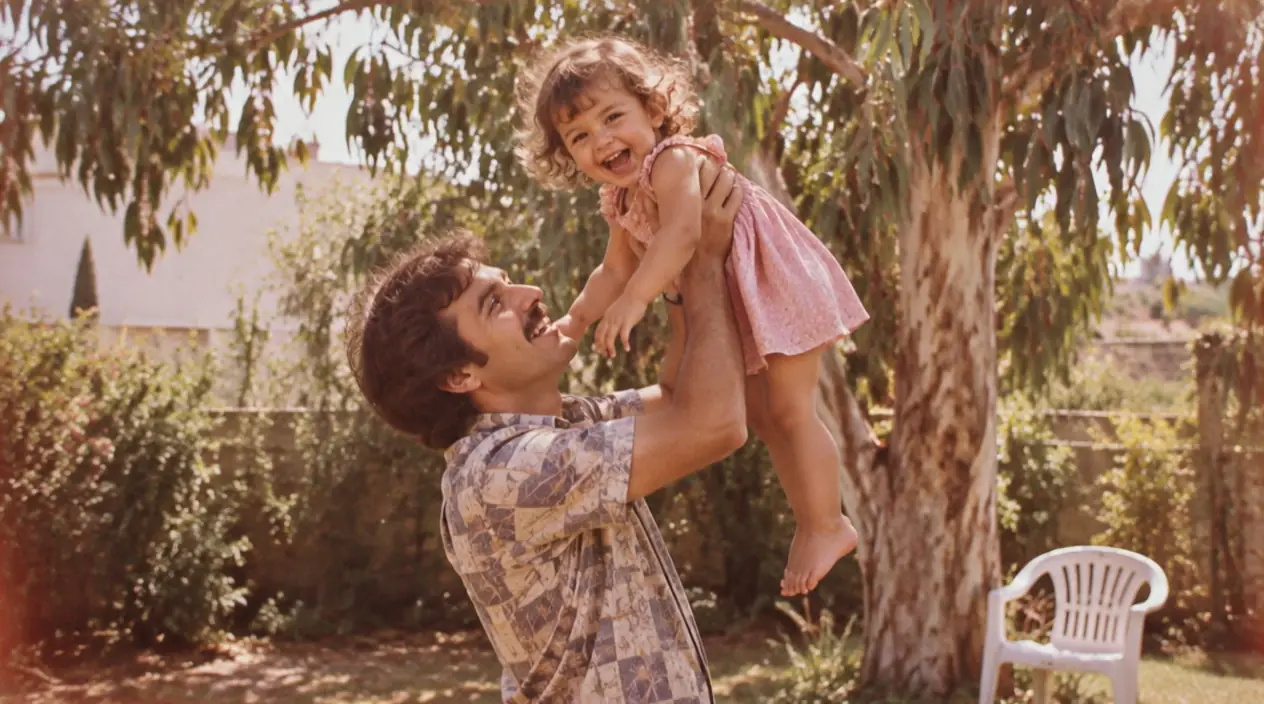 התמונה מ־1979: אב מרים את בתו הפעוטה בגינה, מתחת לעץ אקליפטוס.