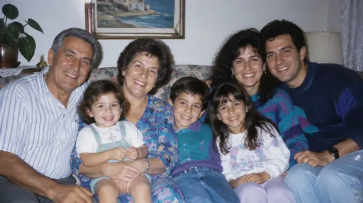 תמונה משפחתית מ־1992: סבא, סבתא, ההורים ושלושה ילדים קטנים על ספה פרחונית בסלון.